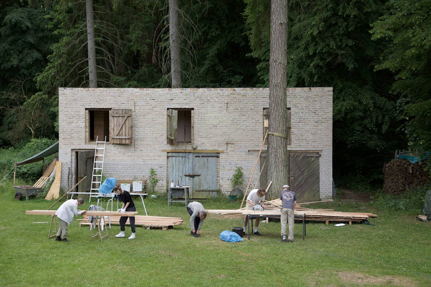 People working with wood in front of a building in nature surrounding.